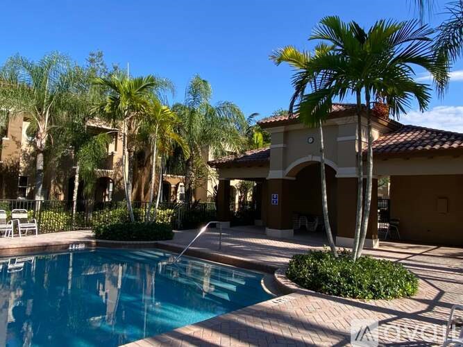 A pool surrounded by palm trees and a building in the background.