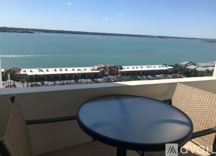 A table and chairs are set up on a balcony overlooking a parking lot and a body of water.