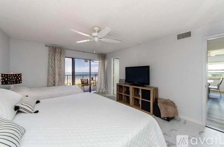A bedroom with a large bed, a television, and a balcony with a view of the ocean.