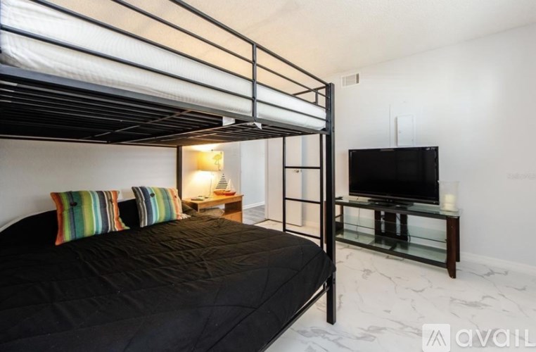 A bedroom with a black bed and a television on a glass table.