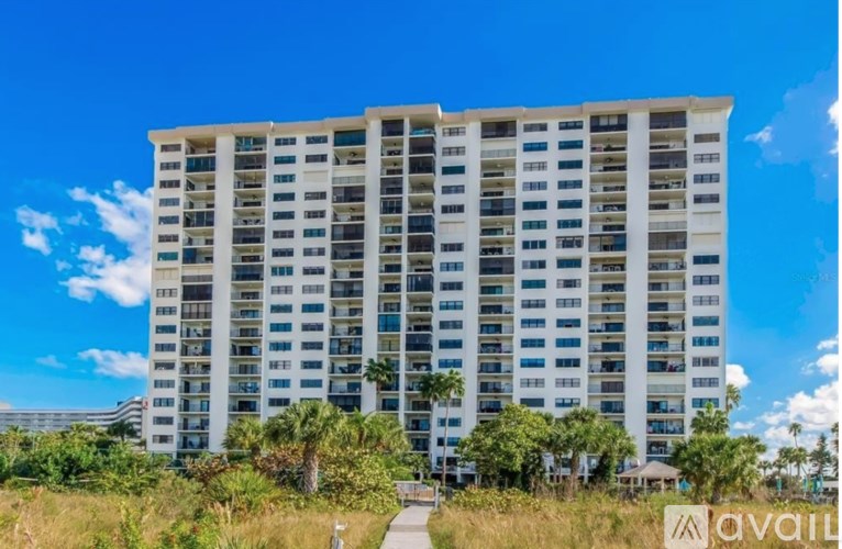 A tall white building with many windows and palm trees in front.