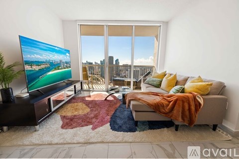 A living room with a flat screen TV and a couch with a blanket on it.