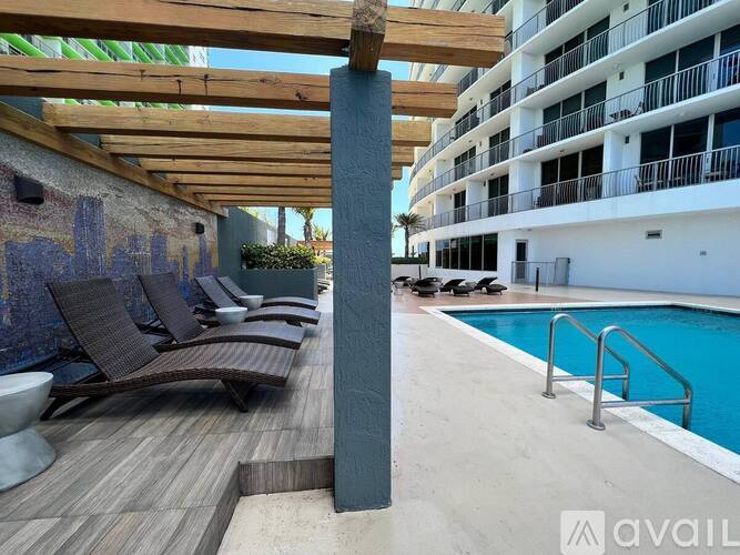 A wooden deck with lounge chairs and a pool next to a tall building.