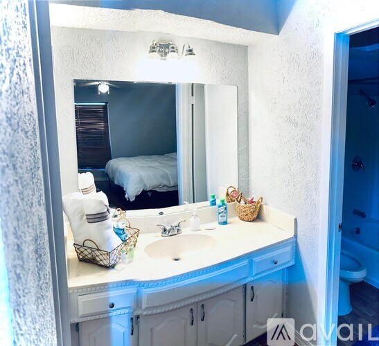 A bathroom with a white counter and a mirror reflecting a bed.