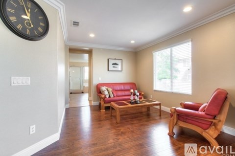 A living room with a red couch and a large clock on the wall.