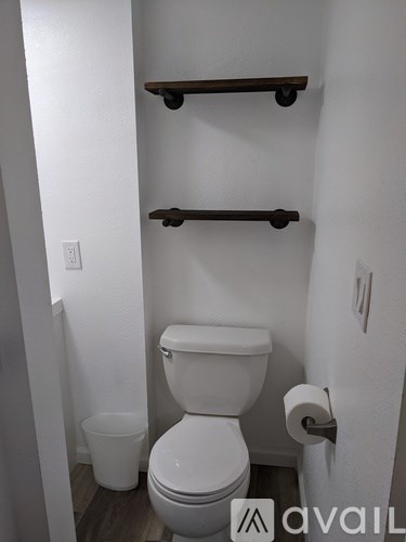A white toilet in a small bathroom with a shelf above it.
