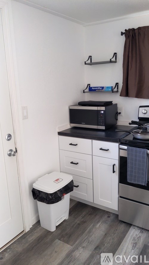A kitchen with a white door, a black microwave, and a white trash can.