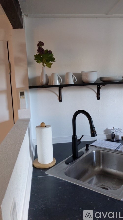 A kitchen with a sink and a shelf with cups and bowls.