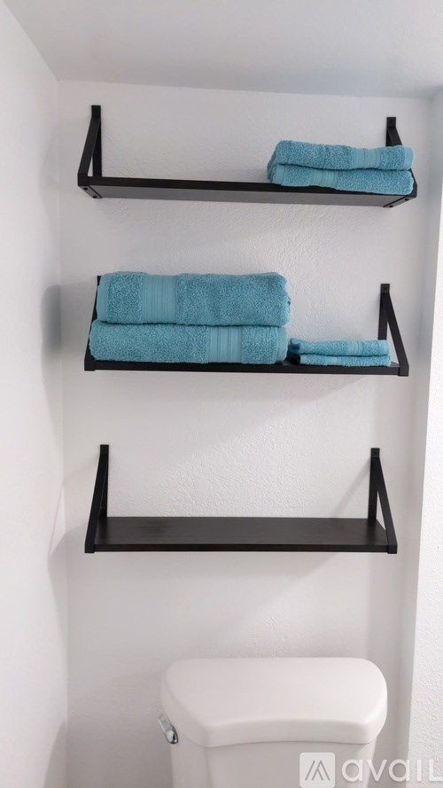 A white toilet is under a shelf with towels on it.