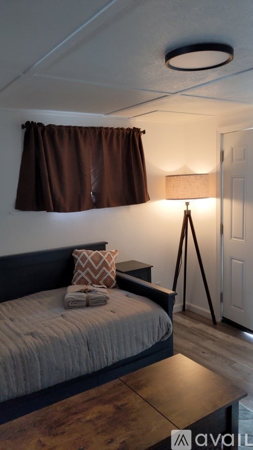 A bedroom with a bed, a lamp, and a window with brown curtains.