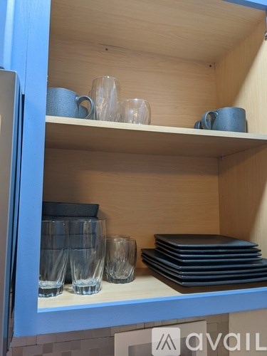 A kitchen cabinet with glasses and plates on the shelf.