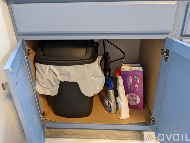 A black trash can with a white cover is in a cabinet under a white drawer.