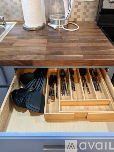 A kitchen counter with a wooden top and a drawer full of utensils.