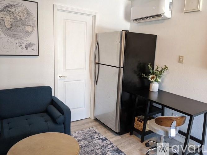 A black fridge stands in a room with a blue couch and a wooden table.