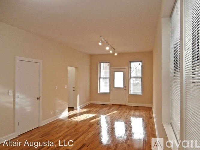 A spacious room with wooden floors and white walls, with a window on the right side.