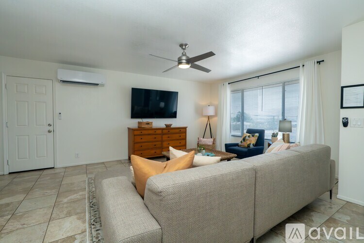 A living room with a grey couch, a flat screen TV on the wall, and a ceiling fan.