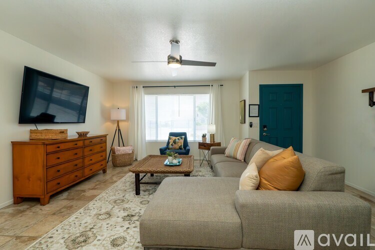 A living room with a grey couch, a wooden dresser, a coffee table, and a ceiling fan.