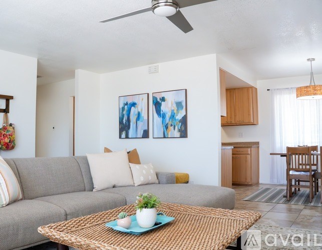 A living room with a grey couch, a woven coffee table, and two abstract paintings on the wall.