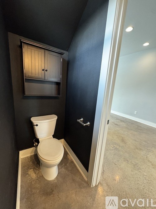 A white toilet in a bathroom with a black wall and a cabinet above it.