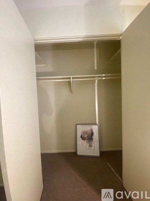 A white picture frame with a painting of a bird is on the floor of a white hallway.