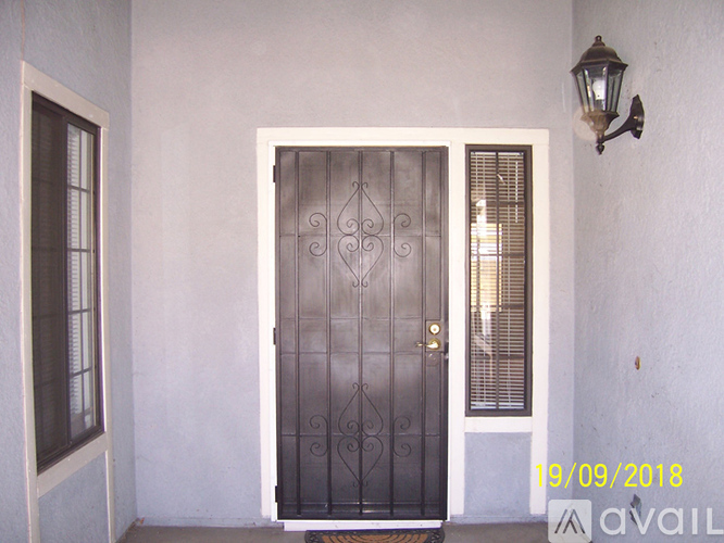 A black wrought iron door with a gold handle is set in a white wall.
