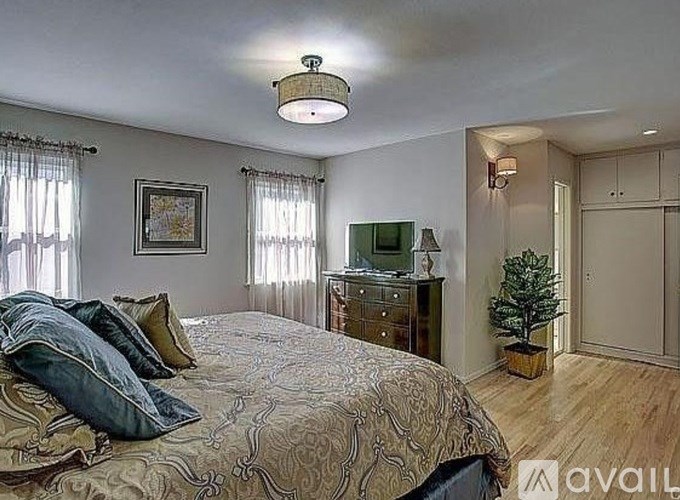 A bedroom with a large bed, a dresser, and a window with curtains.