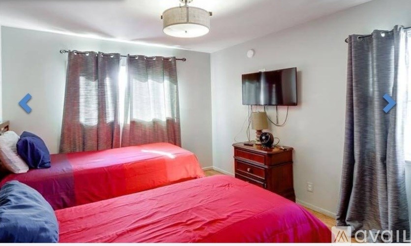A bedroom with a red bedspread and a television on a wooden stand.