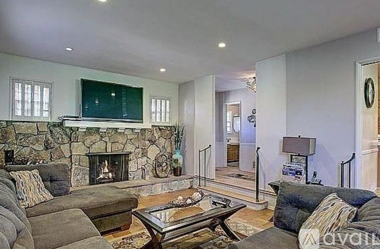 A living room with a stone fireplace and a glass coffee table.