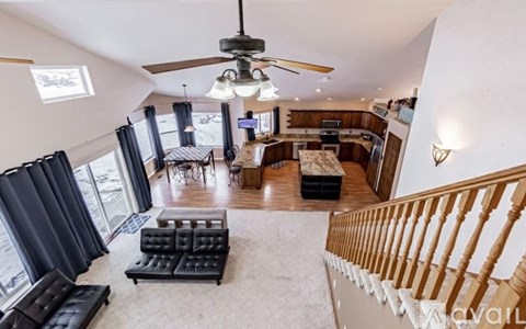 A living room with a black leather couch and a ceiling fan.