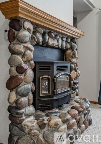 A fireplace with a wooden mantle and a black firebox is surrounded by a stone wall.