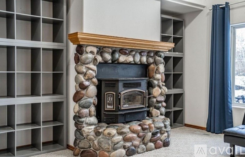 A stone fireplace with a wood mantle is in a room with a window.