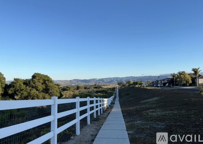 A white fence runs along a path in a grassy area.