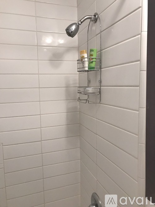 A shower head with a rack of toiletries underneath it.