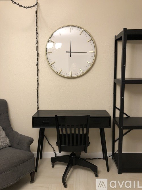 A black desk with a chair and a clock hanging on the wall.