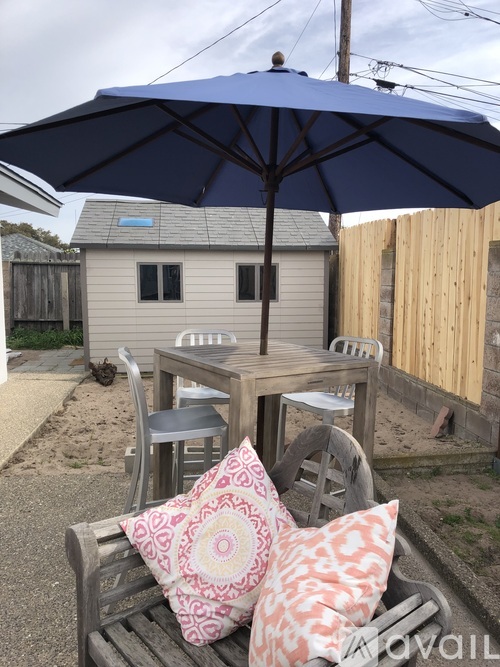 A blue umbrella is on a wooden table with two pillows on a bench.