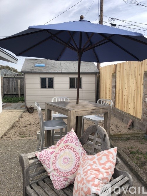 A blue umbrella is on a wooden table with two pillows on a bench.