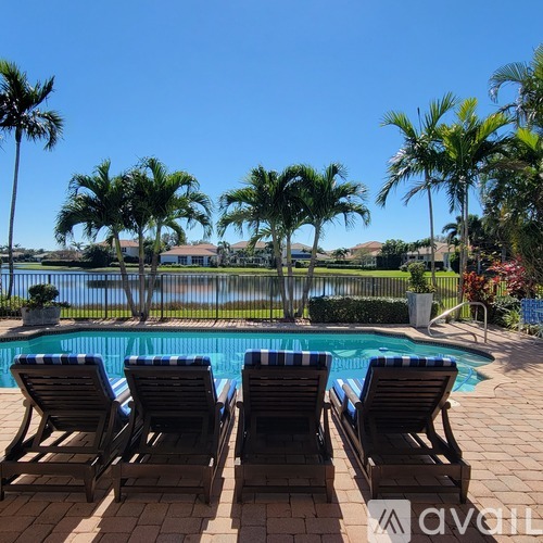 A pool surrounded by palm trees and lounge chairs.