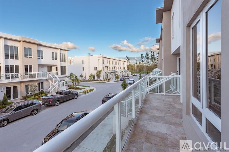 A row of white buildings with balconies overlooking a street with cars parked on the side.