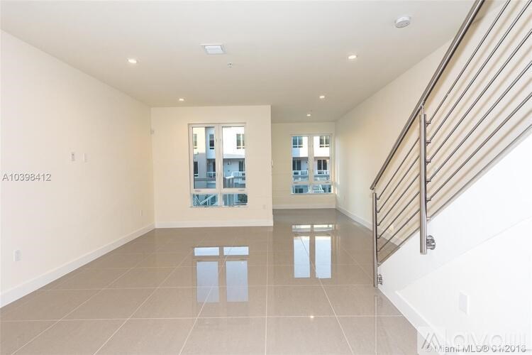 A spacious room with a staircase on the right and a window with a view of a building in the distance.