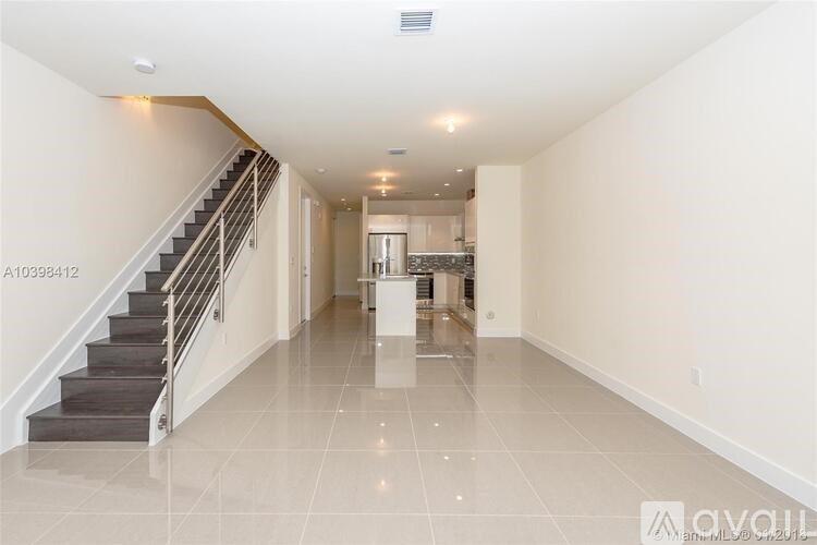 A spacious hallway with a staircase and a kitchen in the background.