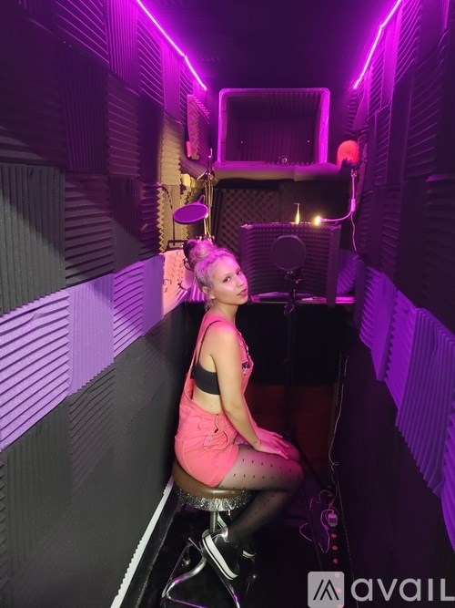 A woman in a pink dress is sitting on a chair in a room with purple lighting.