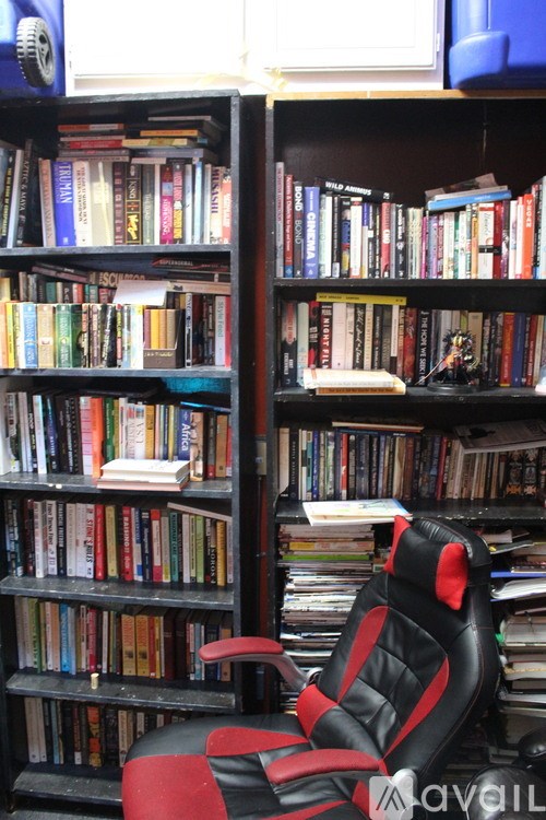 A black and red gaming chair sits in front of a bookshelf filled with books.