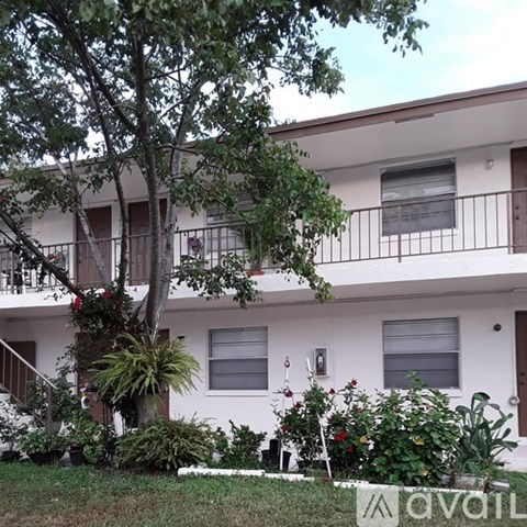 A white building with a balcony and a tree in front.