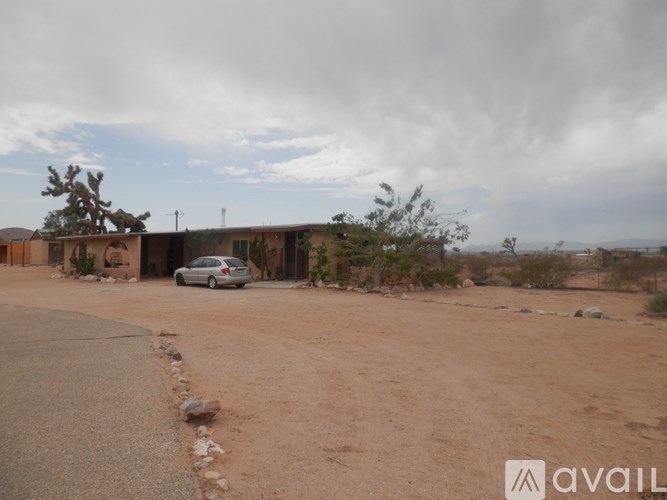 A car is parked in front of a house in a desert-like area.