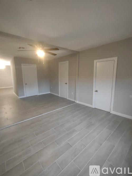 A spacious room with a ceiling fan and light, and a wooden floor.