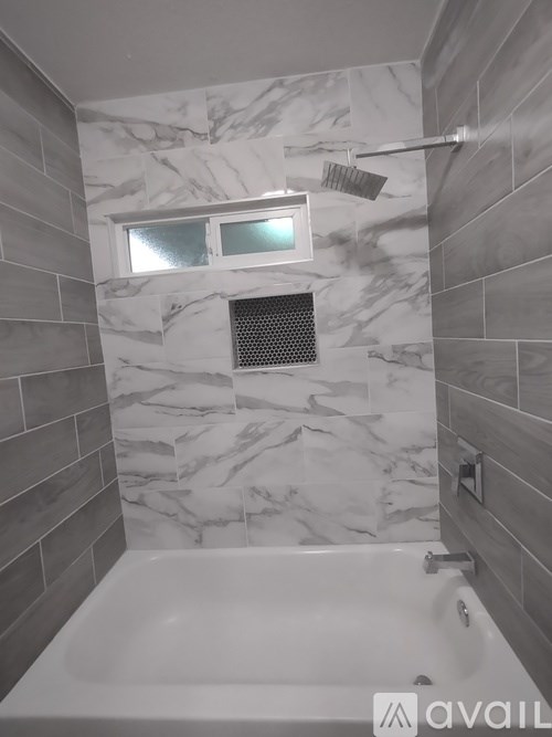 A bathroom with a marble tile wall and a white bathtub.
