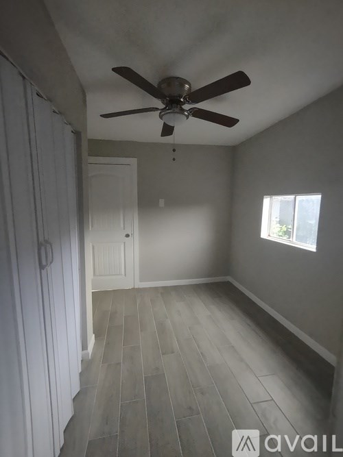A room with a ceiling fan and light, hardwood floors, and a window with blinds.