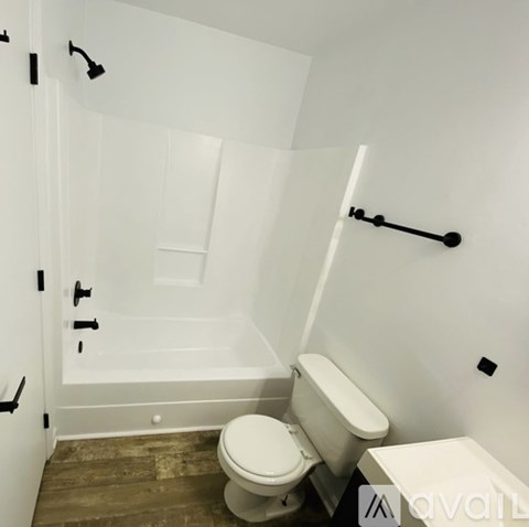 A white toilet sits in a bathroom with a white tub and a white towel.