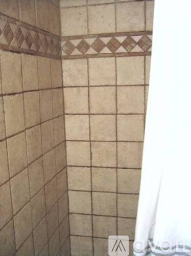 A shower with beige tiles and a brown tile border.