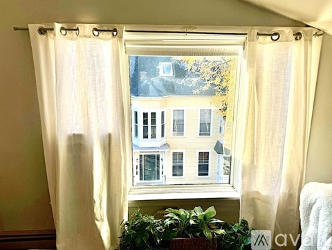 A window with white curtains and a view of a building outside.